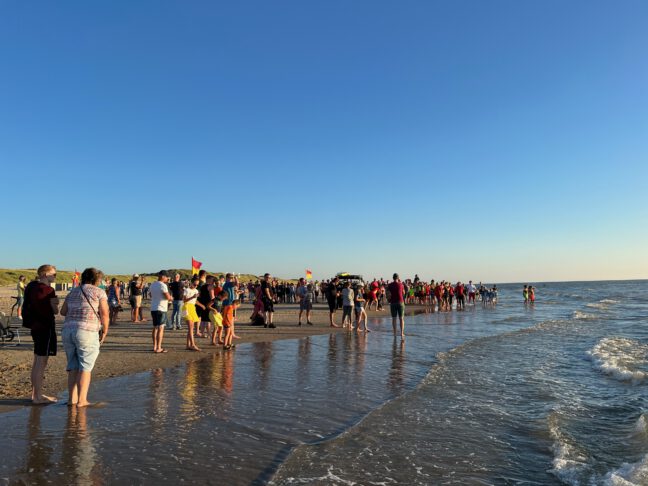 Foto van de demonstratie met een grote groep mensen op het strand die kijken hoe een drenkeling wordt geholpen.